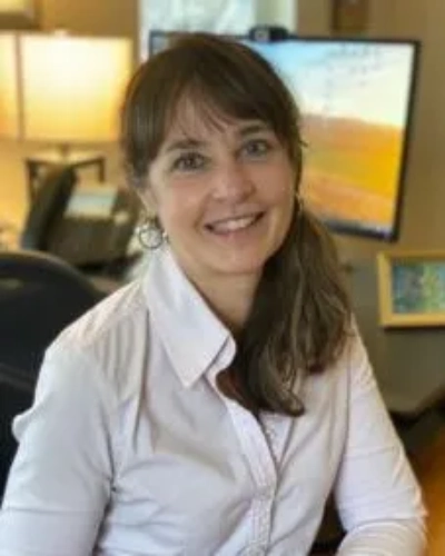 A woman in white shirt and brown tie sitting at desk.